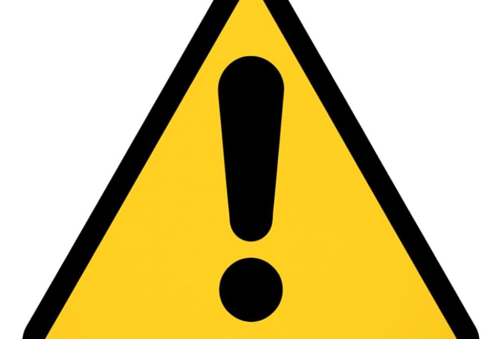 Yellow warning triangle with black exclamation mark symbolizing caution about fake Philips M5070A AED batteries on Amazon.